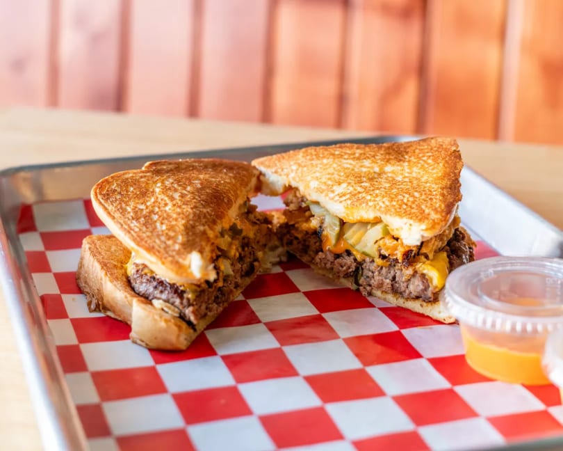 Grilled cheese burger with caramelized onions and cheese on a red and white checkered paper.