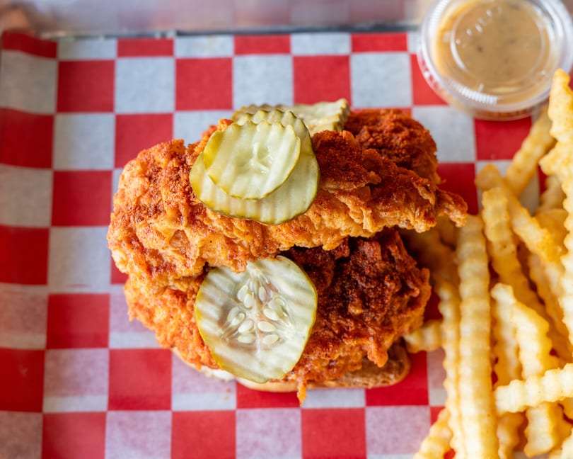 Top-down view of a fried chicken sandwich with pickles, crinkle-cut fries, and dipping sauce.