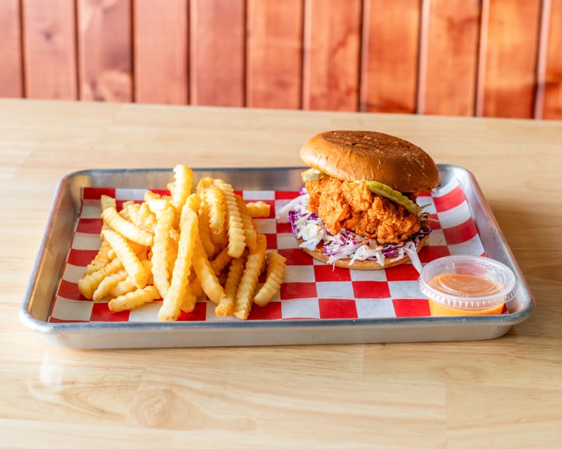 Spicy fried chicken sandwich with coleslaw and pickles, served with crinkle-cut fries and sauce.